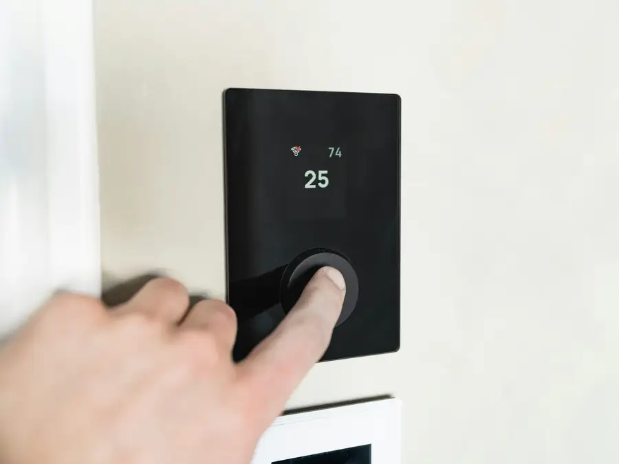 Finger pressing a button on a digital thermostat