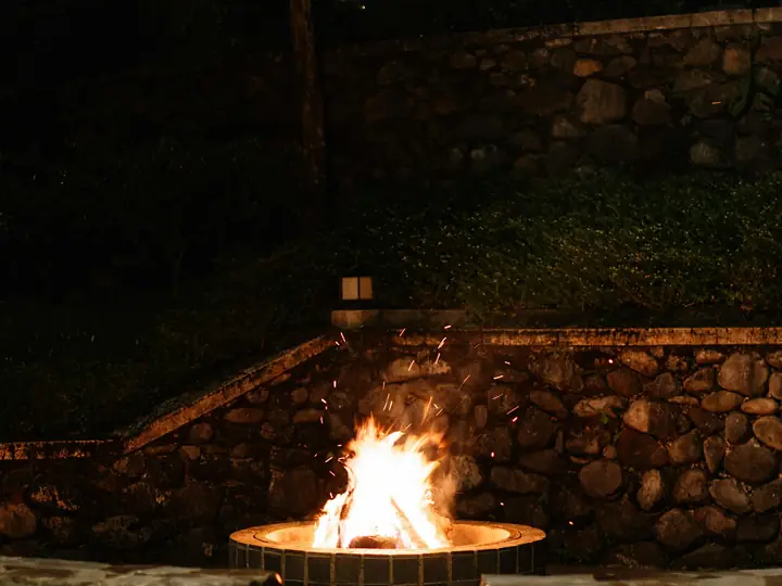 Stone fire pit glowing at night in a landscaped backyard