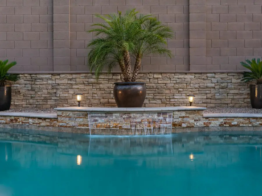 Pool with a stacked-stone wall, potted palms and lights
