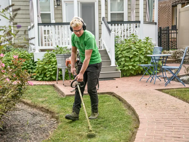 Landscaper trimming grass edges along a brick path