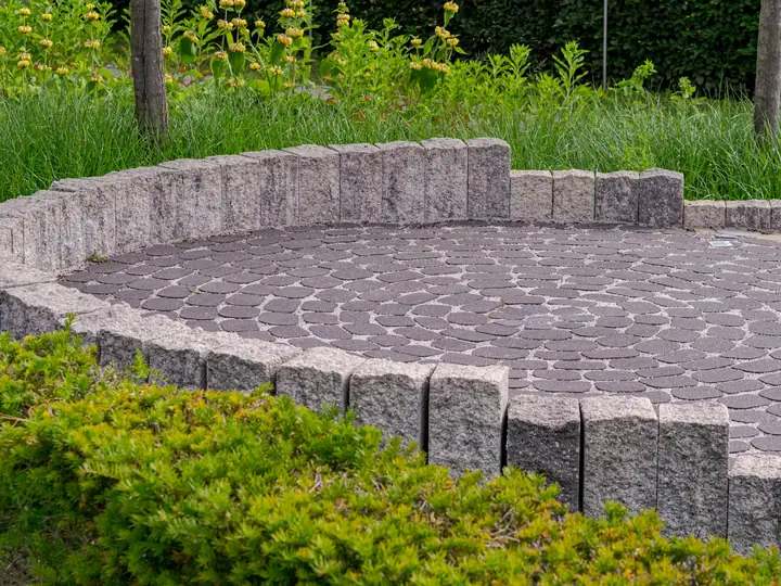 Circular paver patio bordered by stone and green shrubs