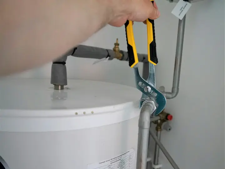 Plumber using pliers on a water heater connection